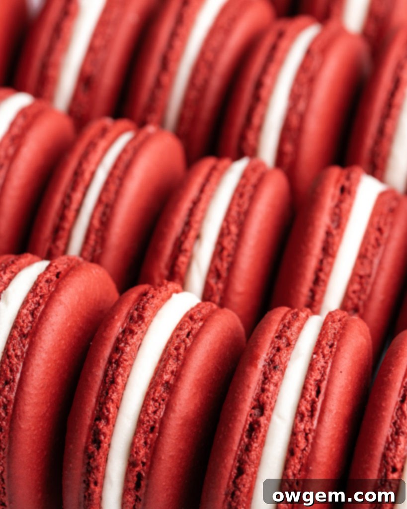 Vibrant red velvet macarons, generously filled with creamy white cream cheese frosting, elegantly arranged on a serving platter, perfect for a special occasion.
