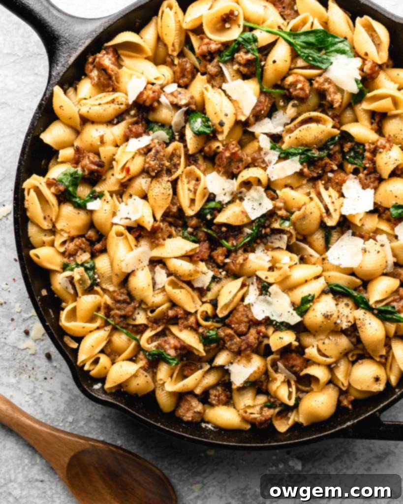 Creamy shell pasta is surrounded by browned crispy sausage, colorful spinach, and delicious pecorino cheese
