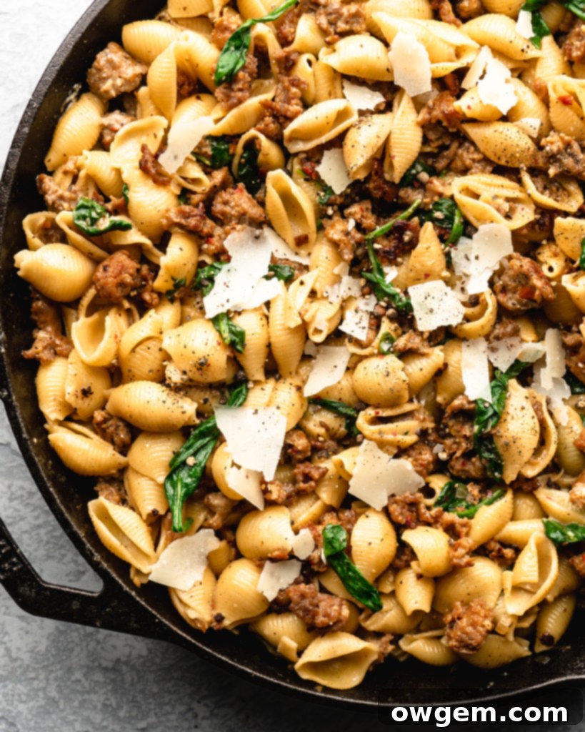Creamy shell pasta is surrounded by browned crispy sausage, colorful spinach, and delicious pecorino cheese