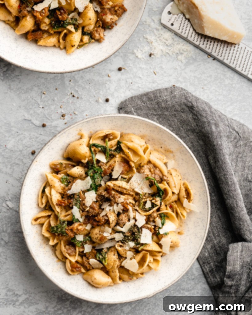 Creamy shell pasta is surrounded by browned crispy sausage, colorful spinach, and delicious pecorino cheese