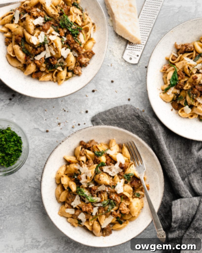 Creamy shell pasta is surrounded by browned crispy sausage, colorful spinach, and delicious pecorino cheese