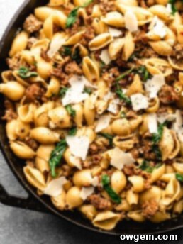 Creamy shell pasta is surrounded by browned crispy sausage, colorful spinach, and delicious pecorino cheese